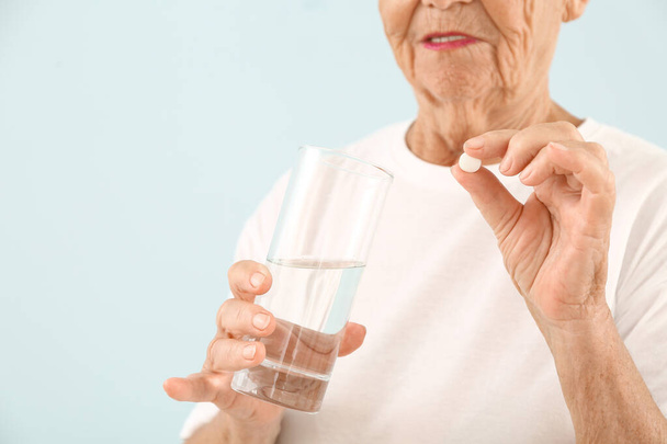 Bejaarde vrouw nemen pil op lichte achtergrond - Foto, afbeelding