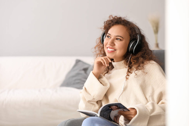 Mulher afro-americana bonita ler revista enquanto ouve música em casa
 - Foto, Imagem