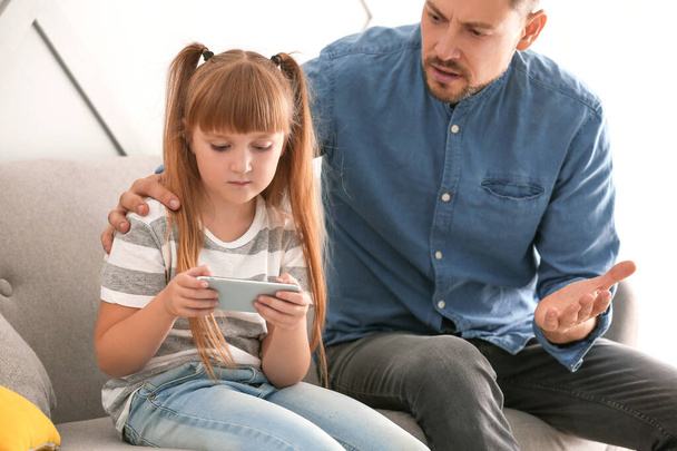 Klein meisje met mobiele telefoon negeren van haar boze vader thuis - Foto, afbeelding