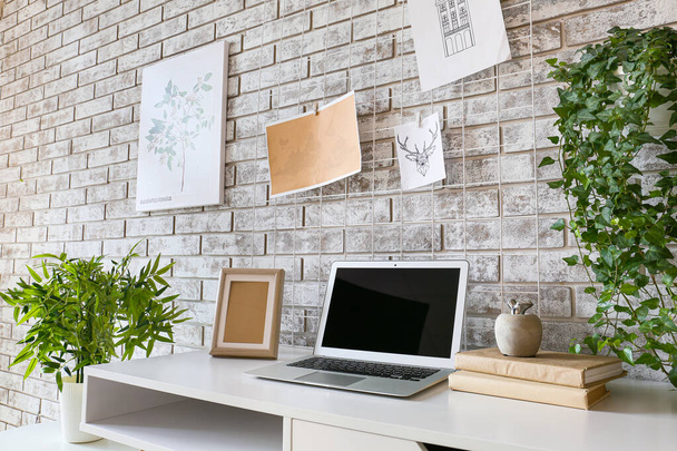 Comfortabele werkplek met stemmingsbord en laptop in de buurt van bakstenen muur - Foto, afbeelding