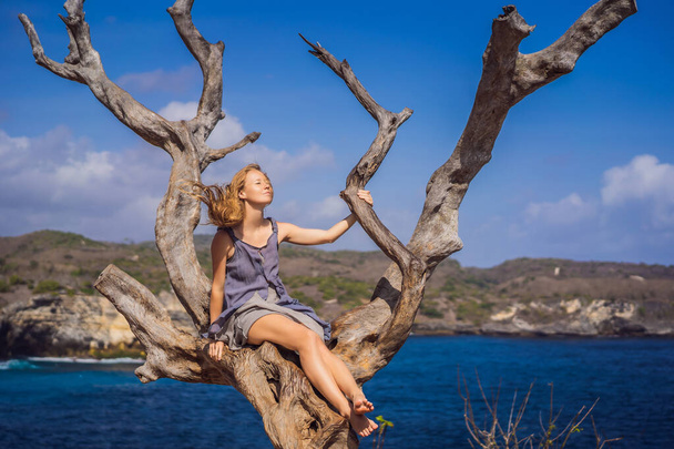 Woman sitting on a tree against the background of the sea Angels Billabong in Nusa Penida, Bali, Indonesia. Bali Travel Concept - Foto, Bild