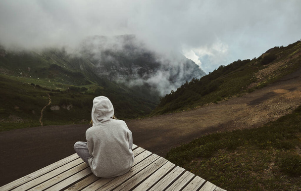 a girl in a grey hoodie sitting on a viewpoint and looking forward - Zdjęcie, obraz