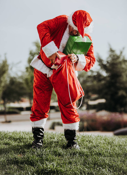 Varastossa kuva Joulupukki ilman partaa seisoo laittamalla lahjoja punaiseen pussiin. Joulun aika
 - Valokuva, kuva