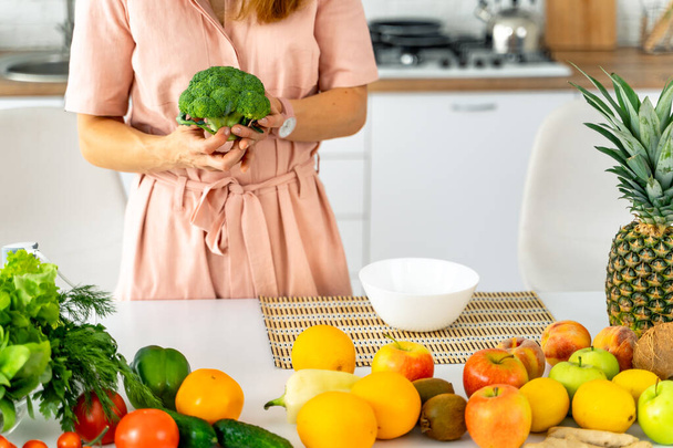 Woman in kitchen ready to prepare meal with vegetables and fruits. Woman with a broccoli. - Foto, Imagen