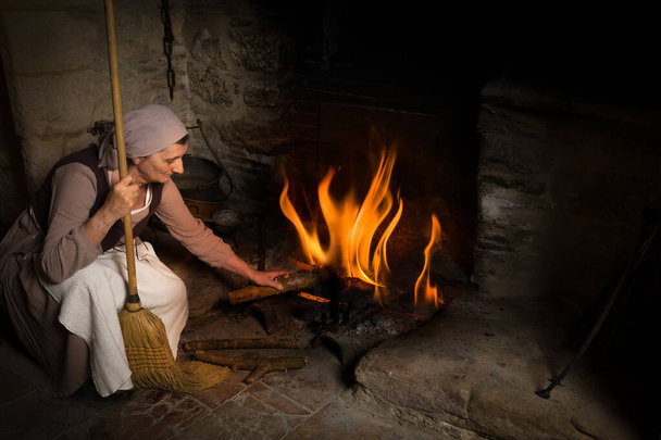 Średniowieczne pokojówka dodając drewna do ognia - Zdjęcie, obraz