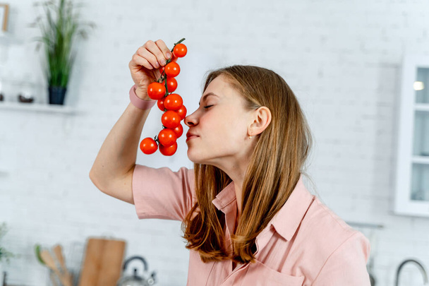 Bando de tomate cereja fresco em mãos de mulher, no fundo da cozinha. Mulher a cheirar tomates. Vegan. Vegeteriano. Alimentos saudáveis
. - Foto, Imagem