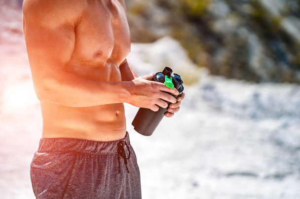 Portrait of a handsome halfnacked bodybuilder man on a mountain with a bottle of water. - Fotoğraf, Görsel
