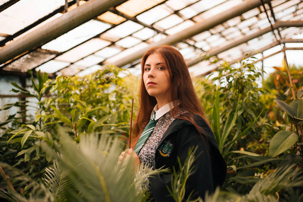 Kopeysk, Chelyabinsk / Russia - 10/02/2019: A girl from the school of young wizards with a magic wand in his hand. A sorceress conjures among plants in a greenhouse, a botany lesson. - Foto, immagini