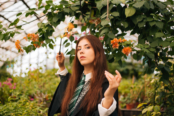A girl from the school of young wizards with a magic wand in her hands. A sorceress conjures among plants in a greenhouse, a botany lesson is cosplay. - Fotografie, Obrázek