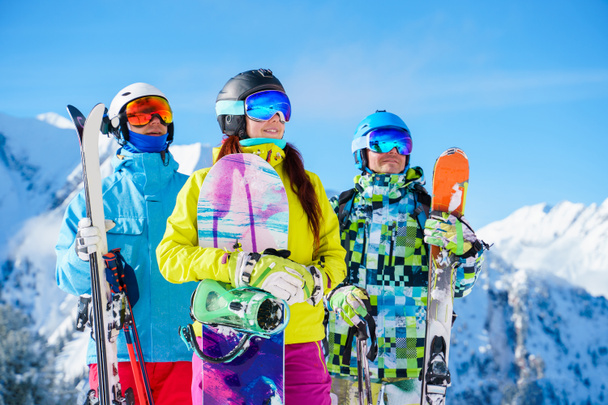 Fotografie sportovkyně a mužů s lyžemi a snowboardem stojící odpoledne v lyžařském středisku - Fotografie, Obrázek