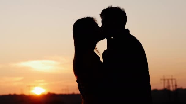 Silhouet van eerste teder kussen van schattig jong paar bij zonsondergang - Video