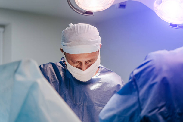 Process of surgery operation using medical equipment. Surgeon in operating room with surgery equipment. Medical background. Closeup of a doctor in medical mask. - 写真・画像