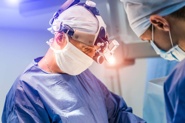 Process of surgery operation using medical equipment. Two surgeons in operating room with surgery equipment and in binocular glasses. Medical background. - Foto, Bild
