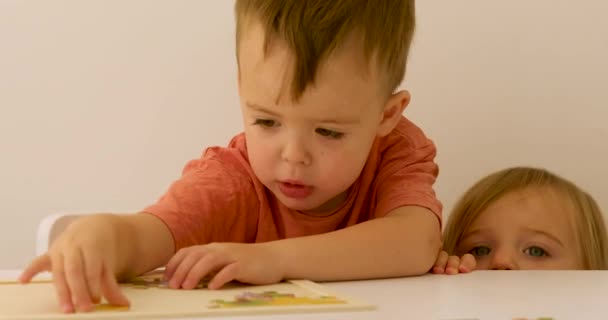 Bir yaşındaki bir çocuk, üç yaşındaki bir çocuğun bulmacayla nasıl oynadığını izliyor. - Video, Çekim