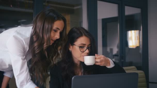 Két nő beszélget egy projektről, egy számítógép képernyőjét nézik az irodában. Két üzletasszony kommunikál munka közben. Irodai munkaterv. - Felvétel, videó