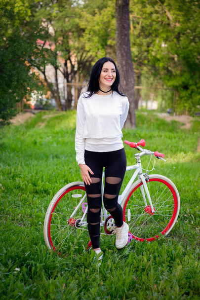 hermosa chica posando en una bicicleta. bicicleta blanca y roja. caminar en la naturaleza. estilo de vida saludable. fin de semana en la naturaleza Retrato de una hermosa chica feliz en una camiseta blanca. lugar para escribir
 - Foto, imagen