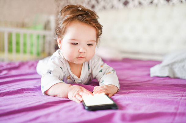 Dipendenza dei bambini dai telefoni. radiazioni dal telefono al bambino. Un bambino 0-1 anni con uno smartphone in mano guarda lo schermo con entusiasmo. Dipendenza gadget bambino
 - Foto, immagini
