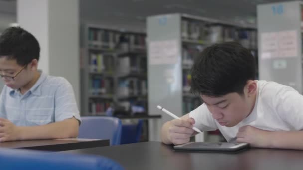 Asiatische Jungen im Vorschulalter nutzen Tablet-Computer in der Bibliothek. Zwei Jungen zeichnen mit Lächeln auf Tablet-Computer. - Filmmaterial, Video