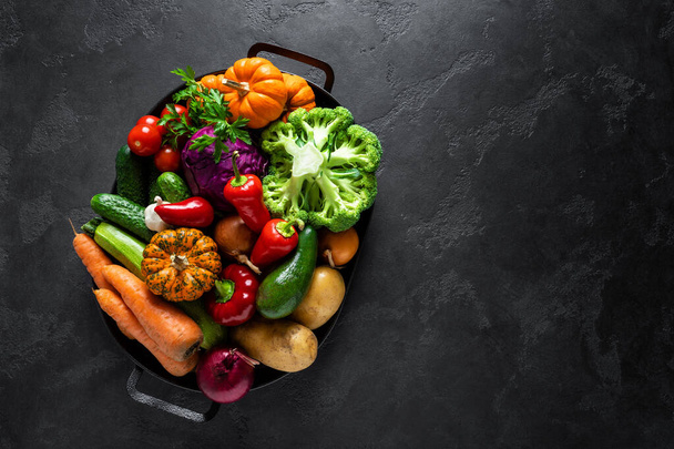 Culinary background with fresh raw vegetables on a black kitchen table, healthy vegetarian food concept, flat lay composition, top view - Foto, afbeelding