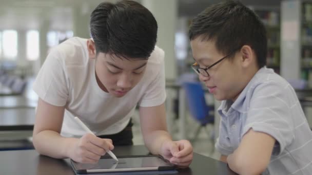 Asiatische Jungen im Vorschulalter nutzen Tablet-Computer in der Bibliothek. Zwei Jungen zeichnen mit Lächeln auf Tablet-Computer. - Filmmaterial, Video