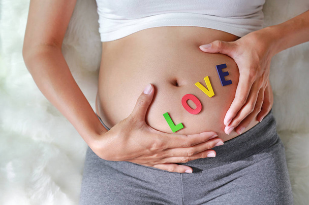 Close up Pregnant woman sitting on soft sofa and touching her belly with sign LOVE in front of her belly. - Photo, image