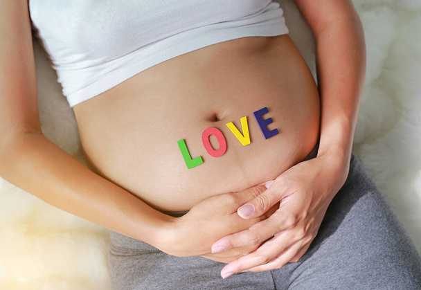 Gros plan Femme enceinte assise sur un canapé doux et touchant son ventre avec signe AMOUR devant son ventre
. - Photo, image