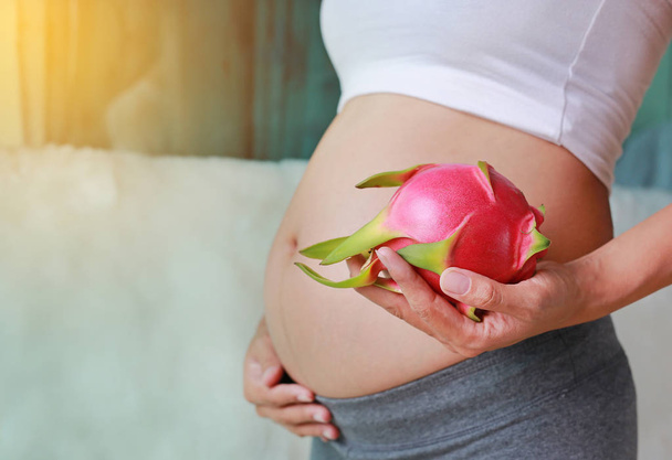 Беременная женщина держит фрукты дракона у живота. Концепция диеты. Здоровый образ жизни
. - Фото, изображение