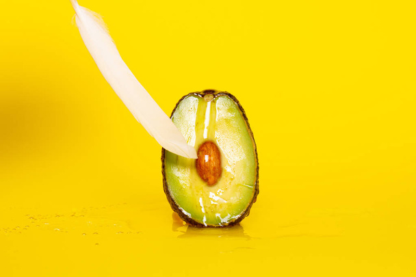 Avocado and feather on red background. Sex game. Foreplay concept.  - Photo, Image