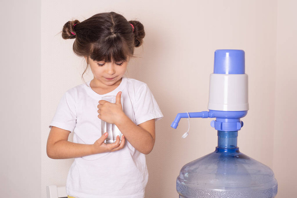 Kind meisje is drinkwater uit handmatige drinkwaterpomp thuis. Watervoorziening thuis concept. - Foto, afbeelding