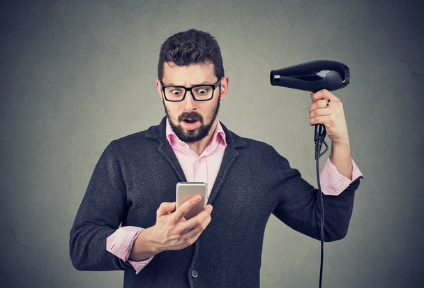 Shocked man checking his phone holding a hair dryer  - Фото, зображення