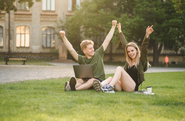 Pari menestyvää nuorta yliopisto-opiskelijaa nostamassa käsiään kahdelle puolelle ylpeinä ja onnellisina nurmikolla istuen. Kaksi iloinen opiskelijoiden kädestä tuntuu voittajia lähellä college kampuksen
. - Valokuva, kuva