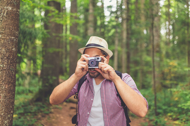 Fashionable backpacker holding vintage film photo camera against forest trees. - Фото, изображение