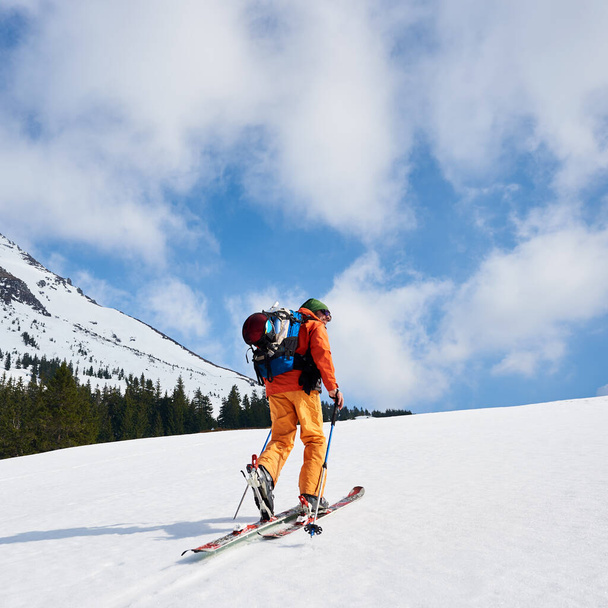 Vuorikiipeilijä kävelee lumisella harjanteella sukset repussaan aurinkoisena päivänä.
 - Valokuva, kuva