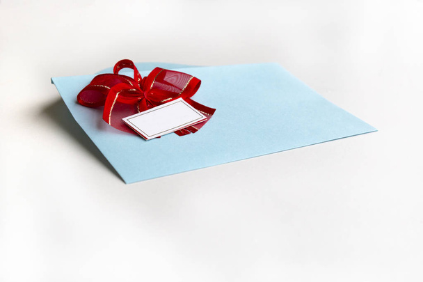Blank paper blue envelope with red ribbon bow, letter for mail on white background, flat lay, top view. Concept postal service or greeting card - Foto, Bild