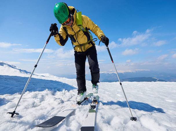 Спортсмен лыжник в шлеме и в очках с рюкзаком катается по крутому снежному склону на фоне копировального пространства голубого неба и красивого горного ландшафта
 - Фото, изображение