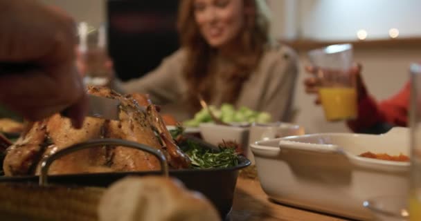 Low angle close up of the hands of a young mixed race man sitting at a table for Thanksgiving dinner at home with friends carving the turkey, a young Caucasian woman talking at the table in the background - Materiaali, video