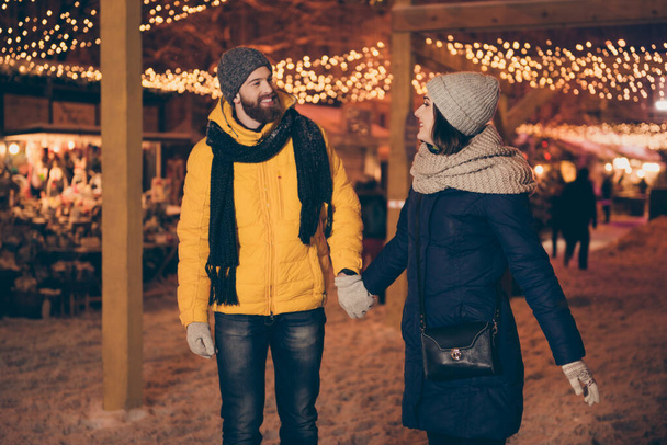Photo of two adorable people guy lady walking lights midnight gifts market newyear evening enjoy snowy weather wear winter coats scarfs hats gloves outdoors - Photo, image