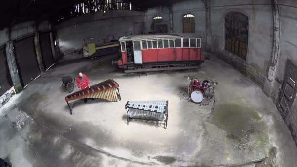 Luftaufnahmen Mann spielt Marimba in rotem Outfit - alte Eisenbahnreparaturfabrik - Filmmaterial, Video