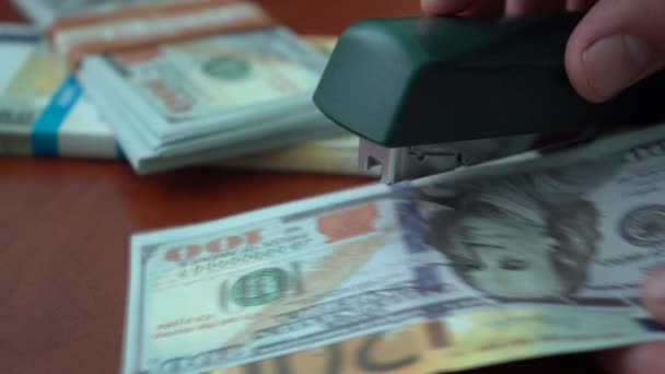The stapler fastens the dollar and euro notes with iron clips. Stapler with paper clips on the background of banknotes. Counterfeit money - Séquence, vidéo