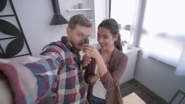 funny guy with girl take selfie video on mobile phone and fooling around with vegetables while cooking salad on brunch for wellness according to diet - Footage, Video