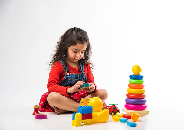 Симпатичная маленькая индийско-азиатская девочка, играющая с симпатичными блочными игрушками на белом фоне
 - Фото, изображение