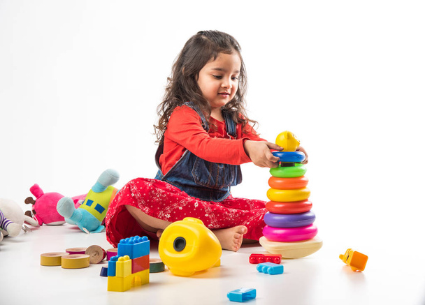 niedliches kleines indisches / asiatisches Mädchen, das mit bunten Blockspielzeugen auf weißem Hintergrund spielt - Foto, Bild