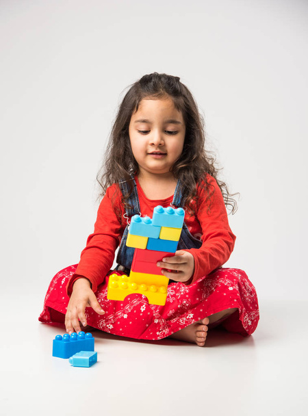 niedliches kleines indisches / asiatisches Mädchen, das mit bunten Blockspielzeugen auf weißem Hintergrund spielt - Foto, Bild