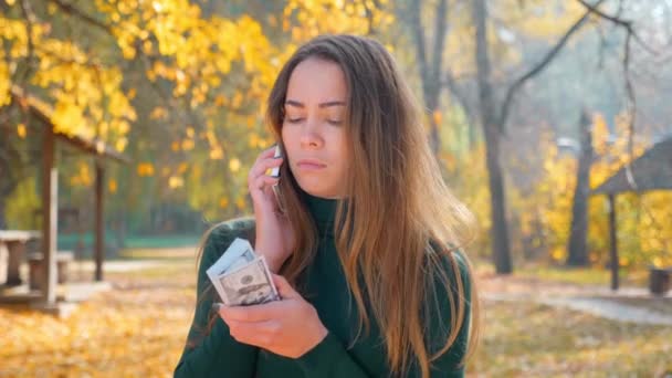 Young attractive brunette woman talking on phone and holding pack of money. Girl enjoys lot of cash. Huge wealth of money. Employee salary. Cash money payment. Successful business concept. 4K footage - Footage, Video