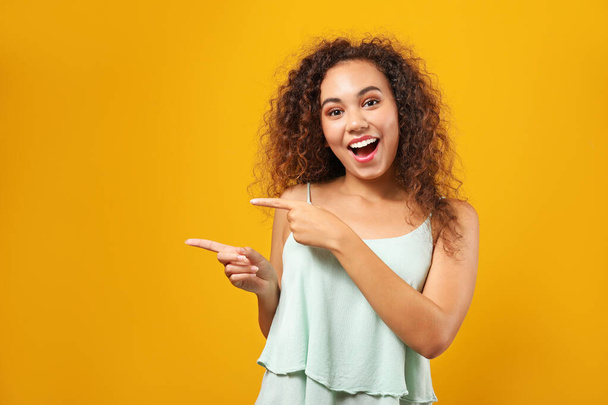 Portrait of happy African-American woman pointing at something on color background - Photo, Image