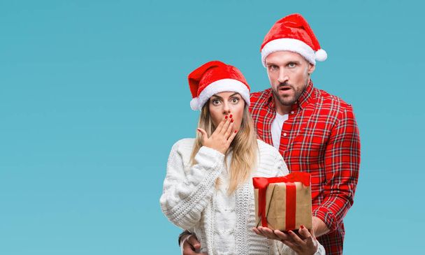 Młoda para w miłości, Boże Narodzenie kapeluszu i trzymając obecny na na białym tle pokrywa usta ręką szoku ze wstydem za błąd, wyrażenie strachu, przestraszony w milczeniu, tajne koncepcja - Zdjęcie, obraz