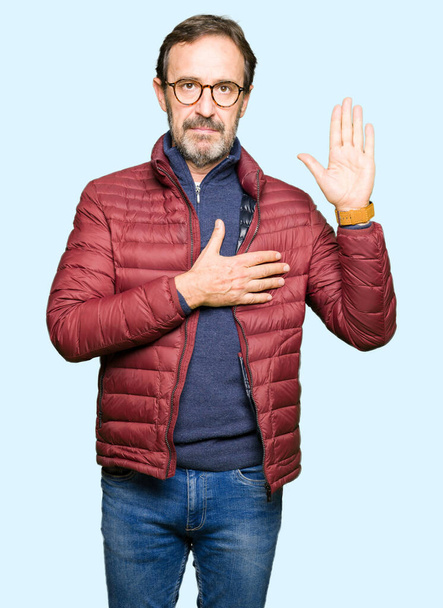 Μέση ηλικία όμορφος άντρας φορώντας γυαλιά και χειμωνιάτικο παλτό ορκίζονται με το χέρι στο στήθος και την ανοιχτή παλάμη, κάνοντας έναν όρκο υπόσχεσης πίστης - Φωτογραφία, εικόνα