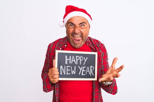 クリスマスの帽子をかぶっている男孤立した白い背景の上に黒板を保持非常に幸せと興奮,大きな笑顔で叫んで勝利を祝う勝者の式と手を上げ - 写真・画像