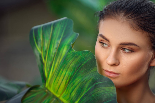 Krásná dívka odpočívá a užívá si dovolenou v tropickém lese. Detailní záběr mladé smyslné brunetky pod palmami. Portrét mladé ženy pózující v blízkosti palmy - Fotografie, Obrázek