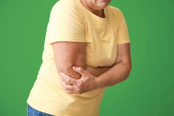 Mujer madura que sufre de dolor en el codo en el fondo de color
 - Foto, Imagen